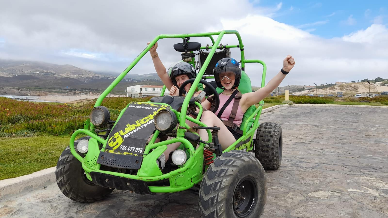 Two riders celebrating in a green Guincho Adventours buggy at the coast