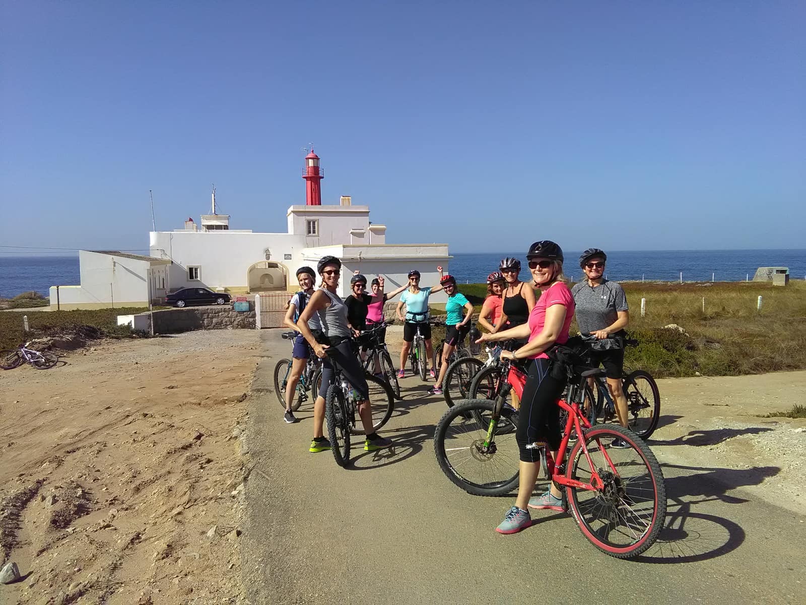 Guided mountain-bike group stopped at a coastal lighthouse with the Atlantic behind