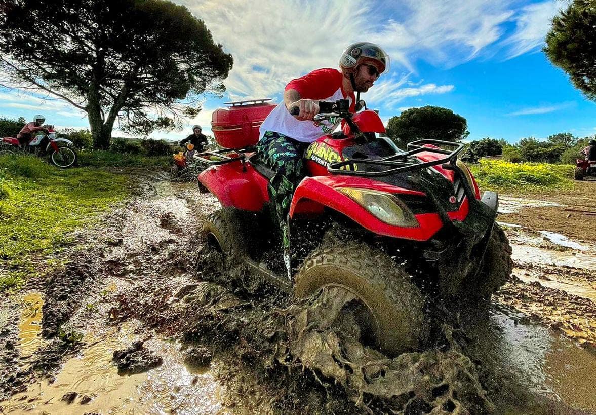 Rider splashing a red quad through mud on the Guincho trails