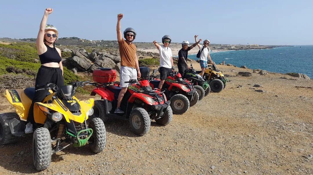 Happy group of Guincho Adventours riders posed on quads at a coastal cliff