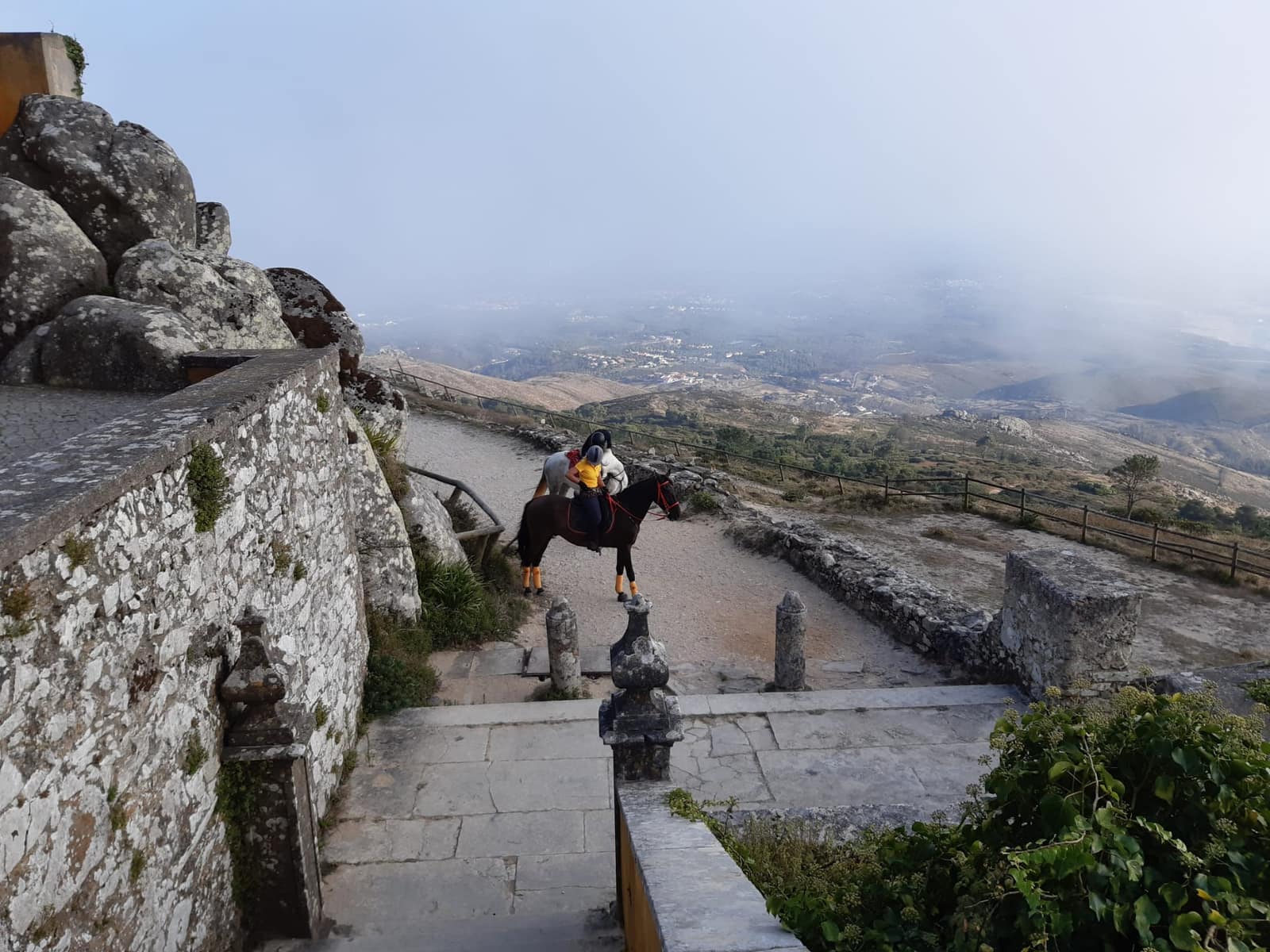 Horseback rider on the Moorish Castle parapet in Sintra, misty hills sweeping down to the coast